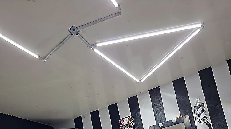 Barras de luz LED en forma de triángulos en el techo blanco, sobre el muro de rayas.